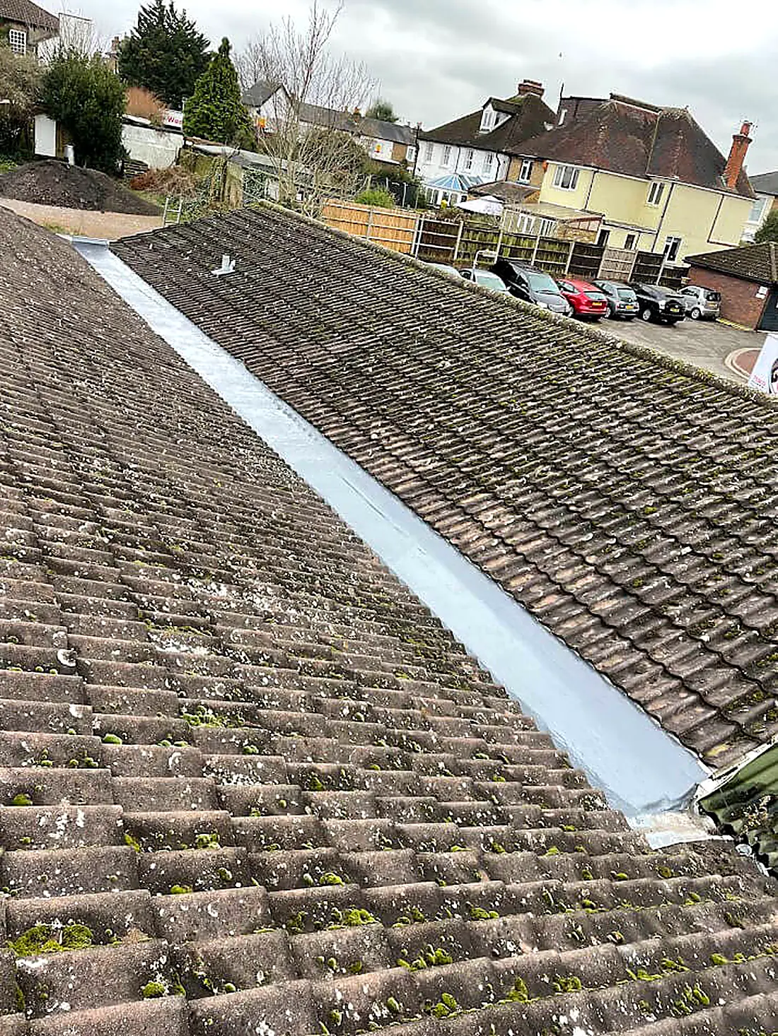 An older mossy tiled roof with a newly lined valley running down it